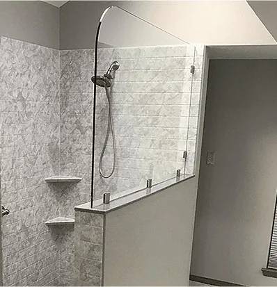 A walk in shower with a half wall and a glass panel